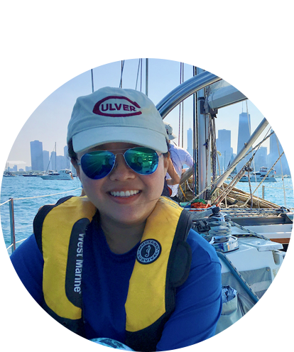 Annie Wang sitting on deck of sailboat with Chicago daytime skyline in background.