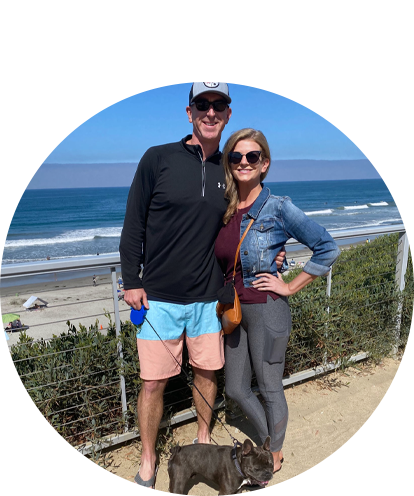 Megan Shaefer fun photo posing with male and small dog with Pacific Ocean in background.