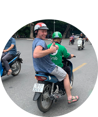 Ben Kagan fun photo riding on back of small motor scooter with thumb up and smiling.