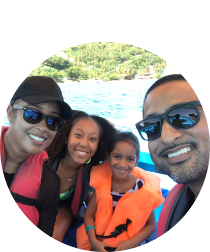 Charisse Williams fun photo posing with adult male, female child, and male child on white water raft wearing life jackets.