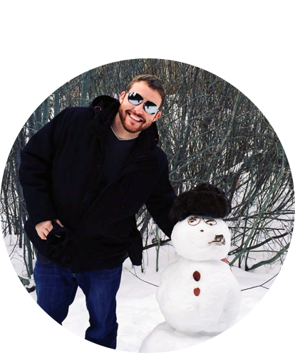 Dan Johnston fun photo posing in winter outside with hand on head of a snowman.