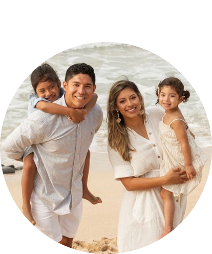 Israel Ramirez posing with family on the beach. Adult female holding young child and adult male holding small child on back.