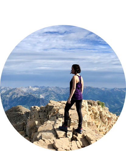 Olivia Riggs standing on top of mountain looking at mountains in the distance.