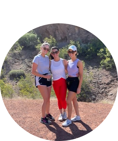 Emily Urban fun photo posing with two other adult females outdoors in active wear on sunny day with desert outcroppings in background.