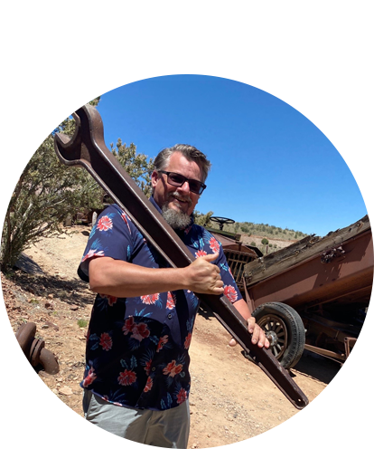 Juc McKillop fun photo posing on sunny day with a giant wrench held over his shoulders.