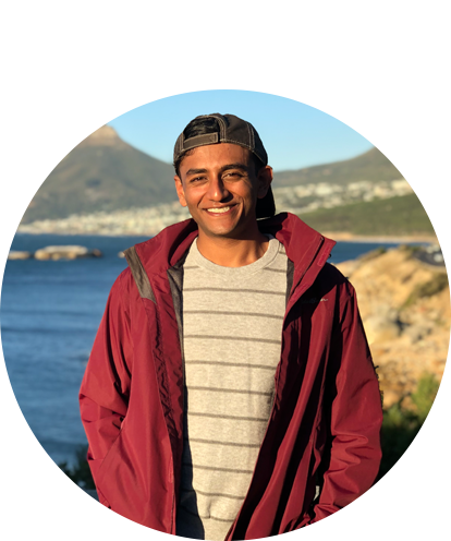 Kevin Mittal fun photo posing in overcoat with waterfront and tall peak in background.