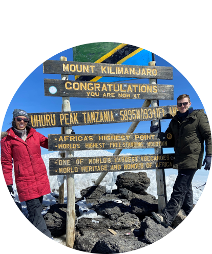 Brandon Nolde fun photo posing with an adult female with a sign marketing the summit of Mount Kilimanjaro.
