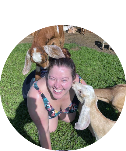 Karaline Feller fun phot on ground with baby goats on her back and one kissing her face.