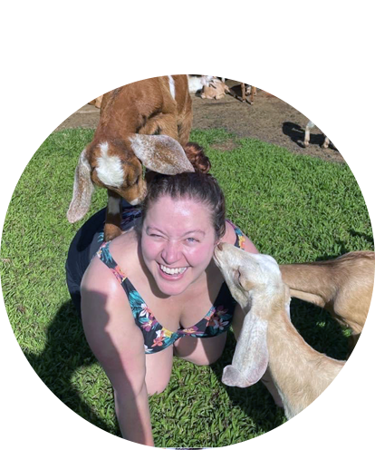 Karaline Feller fun phot on ground with baby goats on her back and one kissing her face.