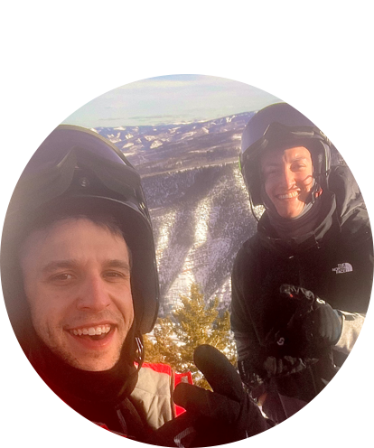 Andrew Salzer fun photo (two adult males in winter outdoor gear with helmets with snow covered mountains in background).